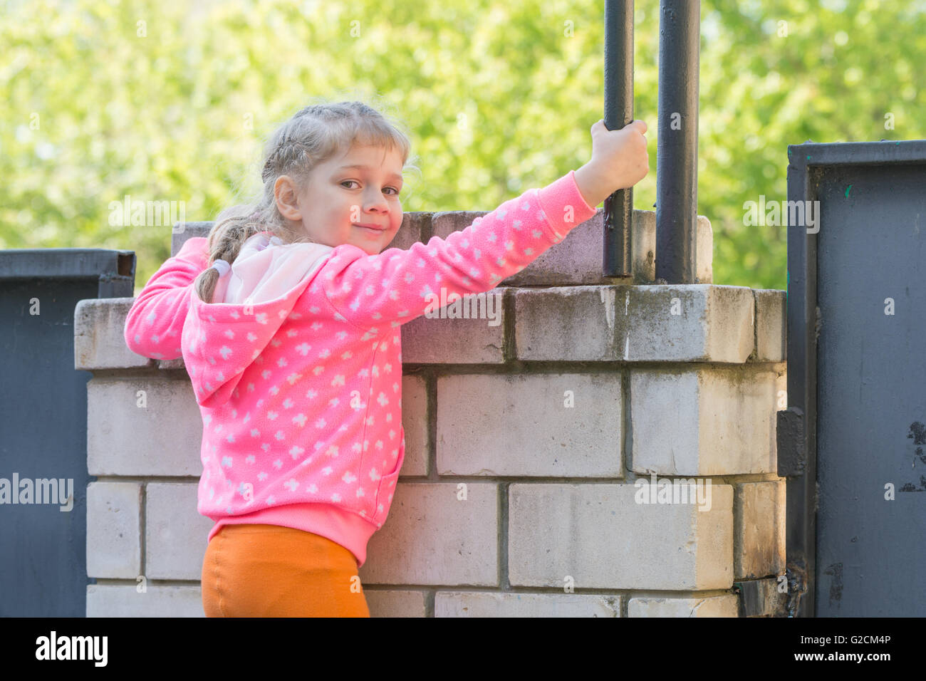 Cinque anni di ragazza è salito su una recinzione di mattoni e si voltò guardato il telaio Foto Stock