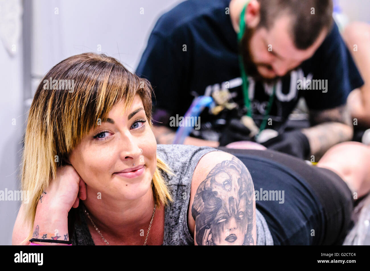 BELFAST, IRLANDA DEL NORD. 28 MAGGIO 2016 - 6th Conferenza del Tattoo dell'Irlanda del Nord. Una cliente femmina sorride mentre ha un tatuaggio sul polpaccio della gamba Foto Stock