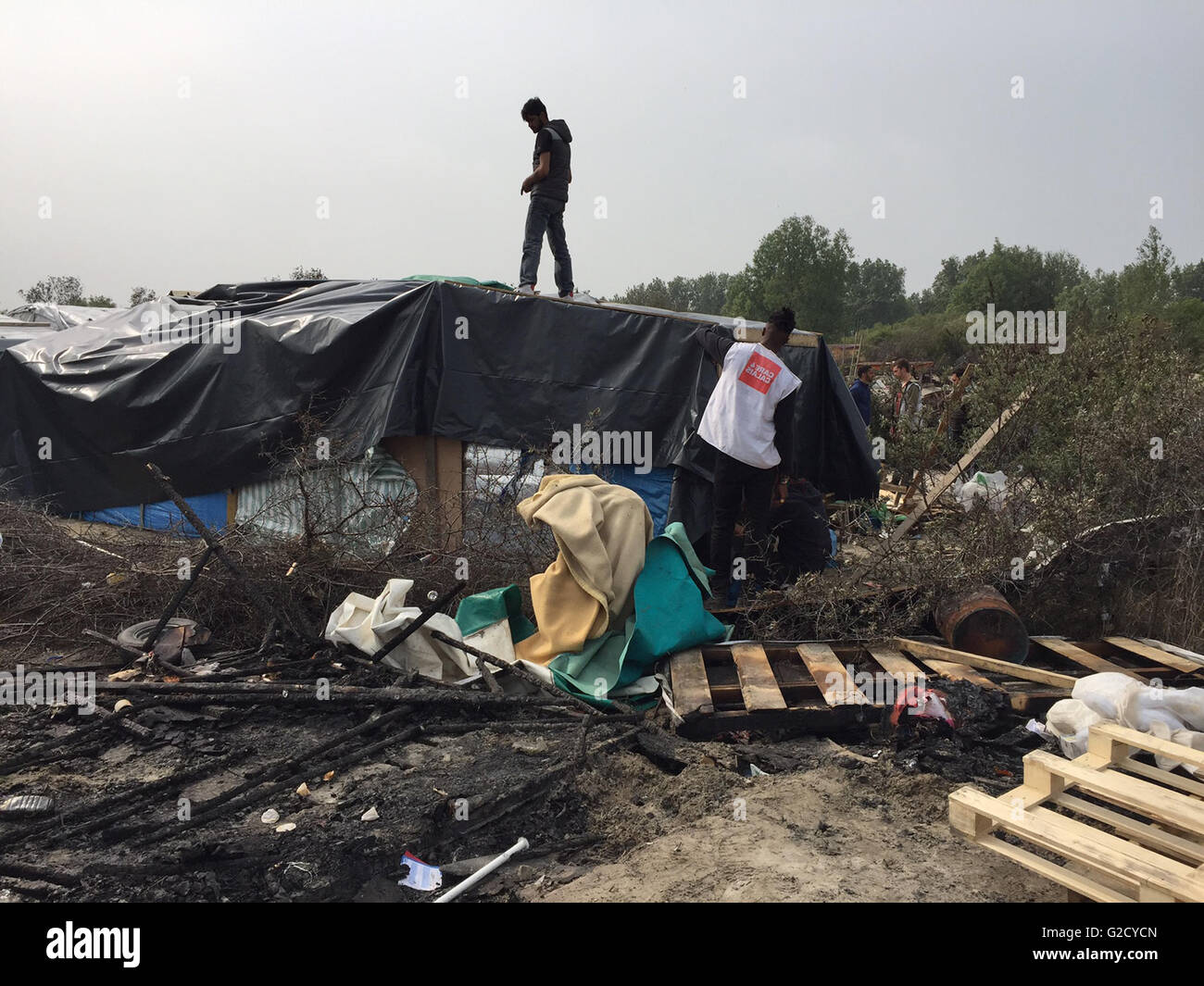Calais, Francia. 27 Maggio, 2016. Un uomo si erge al di sopra dei resti di una capanna di fortuna nel campo migrante soprannominato "Jungle' nella periferia di Calais, Francia, 27 maggio 2016. Quaranta persone sono rimaste ferite in una rissa al campo profughi, le autorità locali ha detto. Diversi rifugi sono stati bruciati. Foto: Anna Psaroudakis/dpa/Alamy Live News Foto Stock