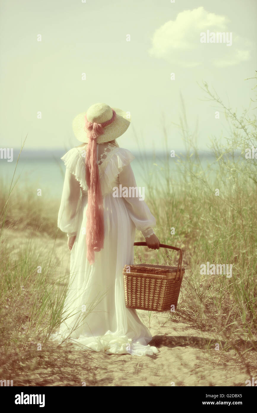 Donna vintage presso la spiaggia con un cestino picnic Foto Stock
