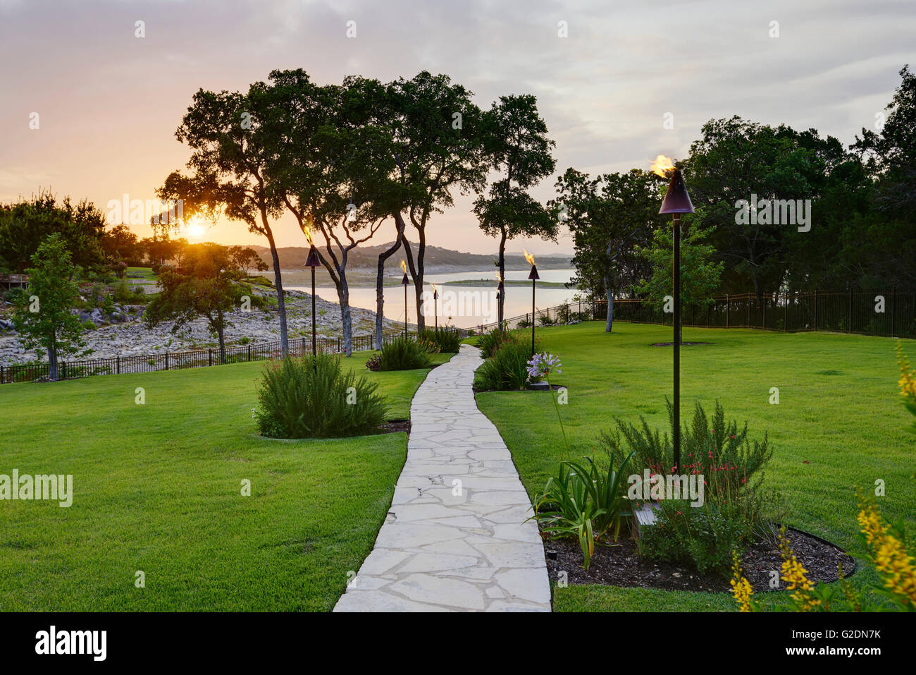 Percorso di pietra ad acqua rivestiti con torce tiki al tramonto Foto Stock