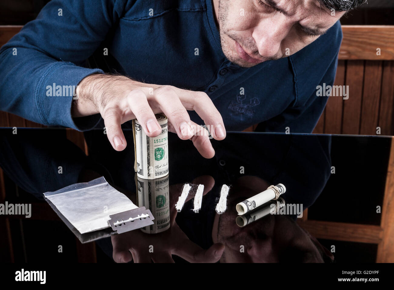 L'uomo bianco grabbing farmaco righe con arrotolato di dollari banconota sul buio con la riflessione Foto Stock