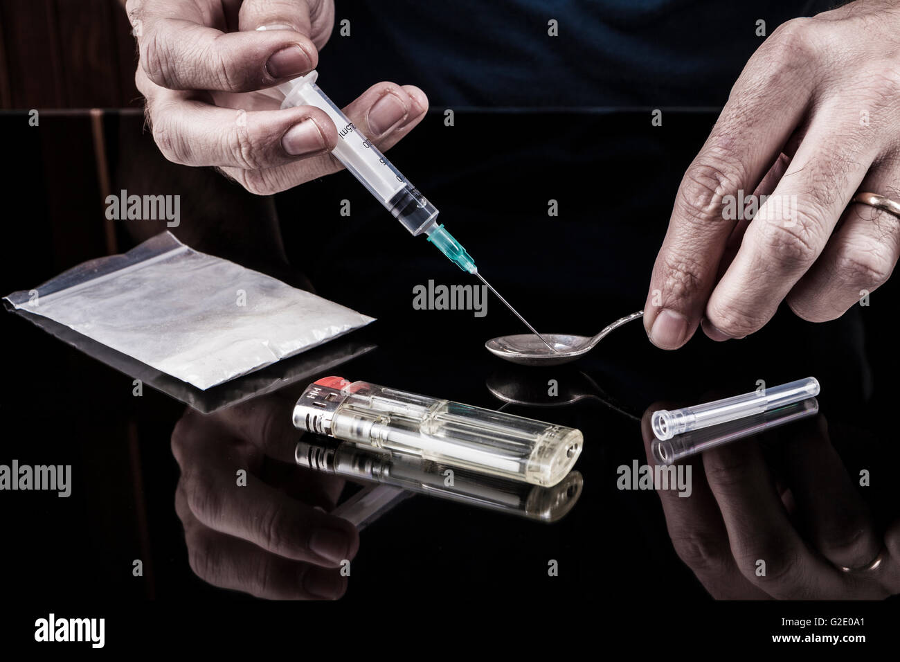 Preparazione di farmaci sul cucchiaino e una siringa su sfondo scuro con la riflessione Foto Stock