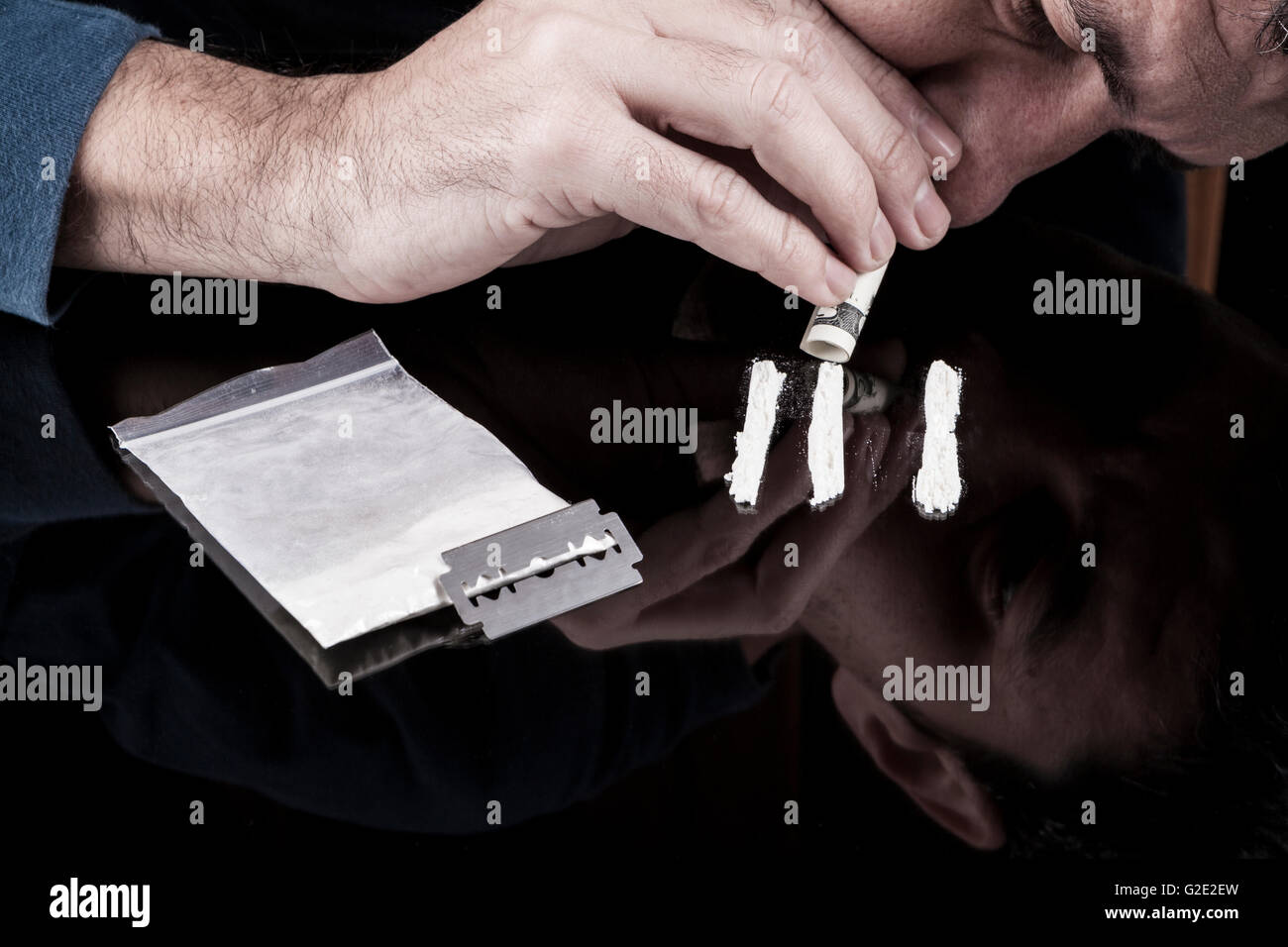 Sbuffare uomo bianco righe di farmaco con arrotolato dollar banconota sul buio con la riflessione Foto Stock