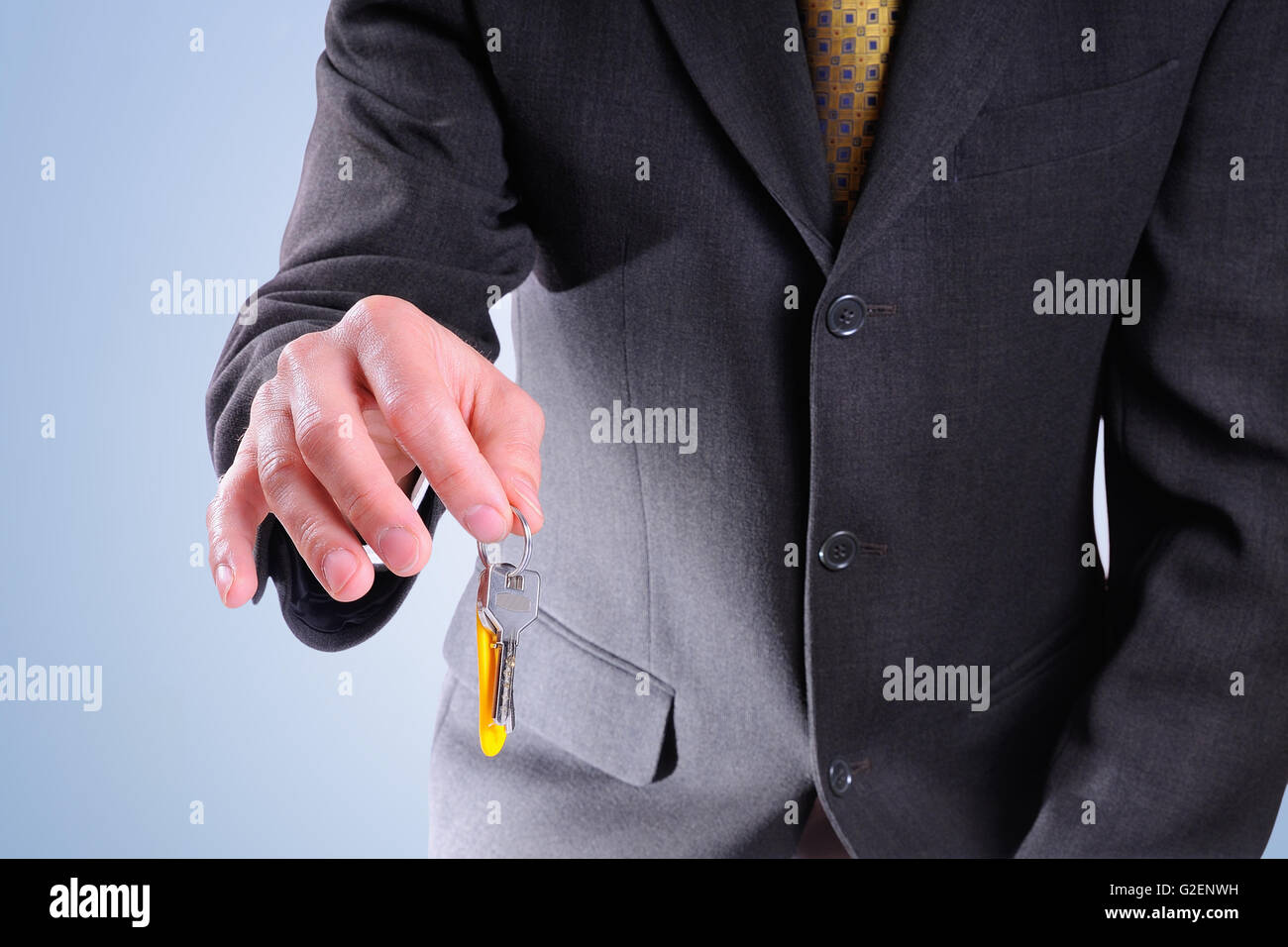 Semi-corpo agente commerciale indossando un grigio scuro costume di consegnare le chiavi per acquisto di una casa con sfondo blu isolare Foto Stock