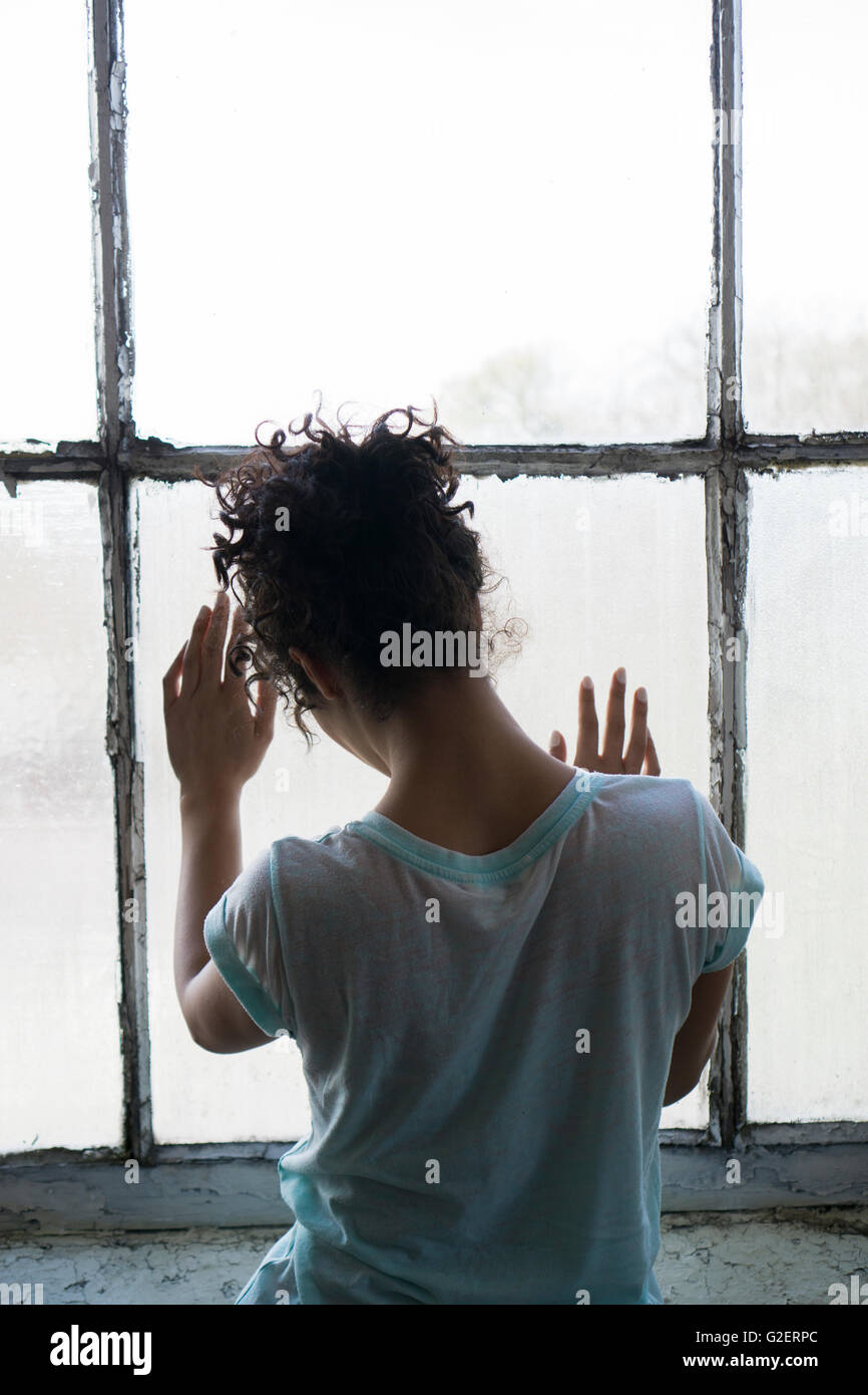 Vista posteriore di una giovane donna in piedi dalla finestra mani toccano il vetro Foto Stock
