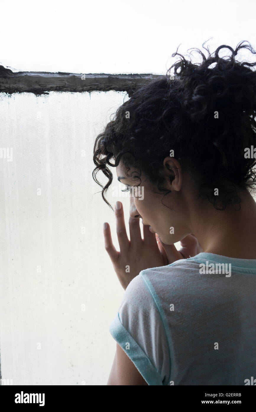 Vista posteriore di una giovane donna in piedi dalla finestra mani toccano il vetro Foto Stock