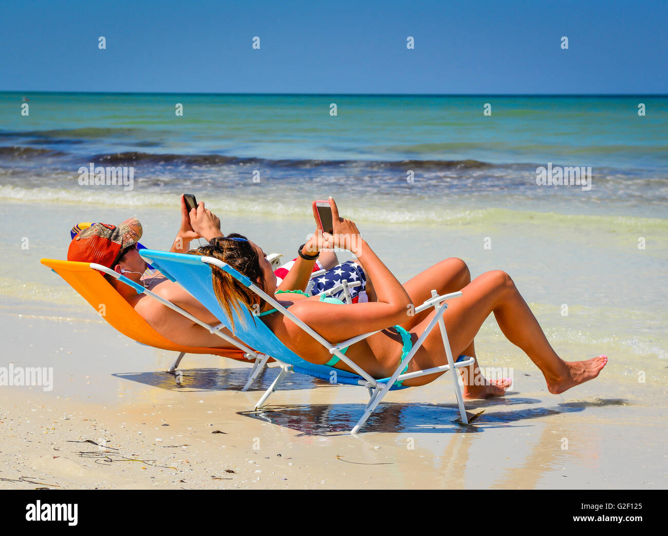 Preoccupato giovane riesco a smettere di guardare i loro telefoni cellulari mentre reclinate in sedie da spiaggia vicino al litorale in spiaggia Foto Stock