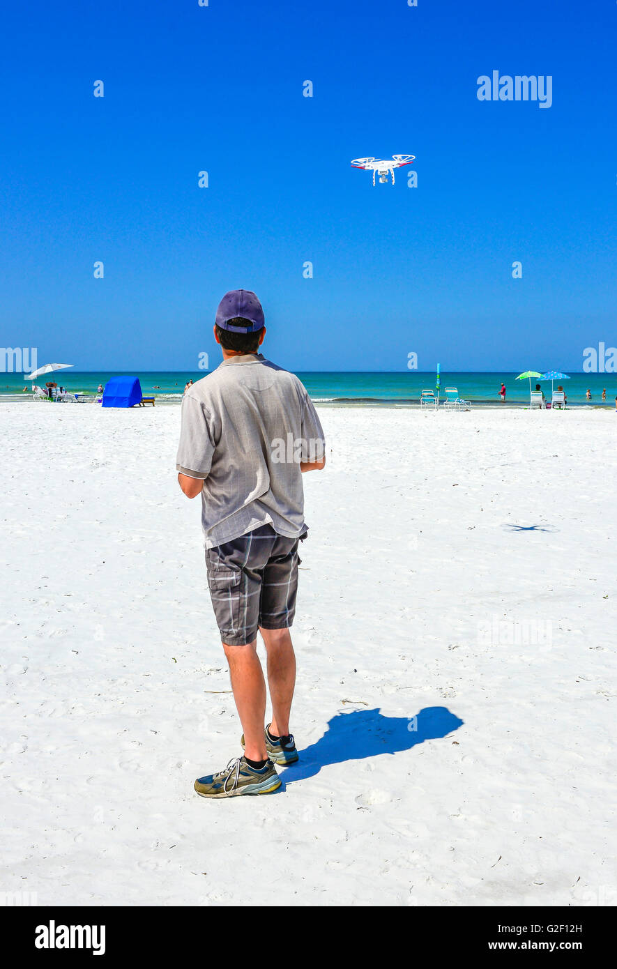 Un non-drone militare aerea vola sulla spiaggia con una vista posteriore del pilota guardando verso il cielo in una giornata di sole con un cielo azzurro Foto Stock