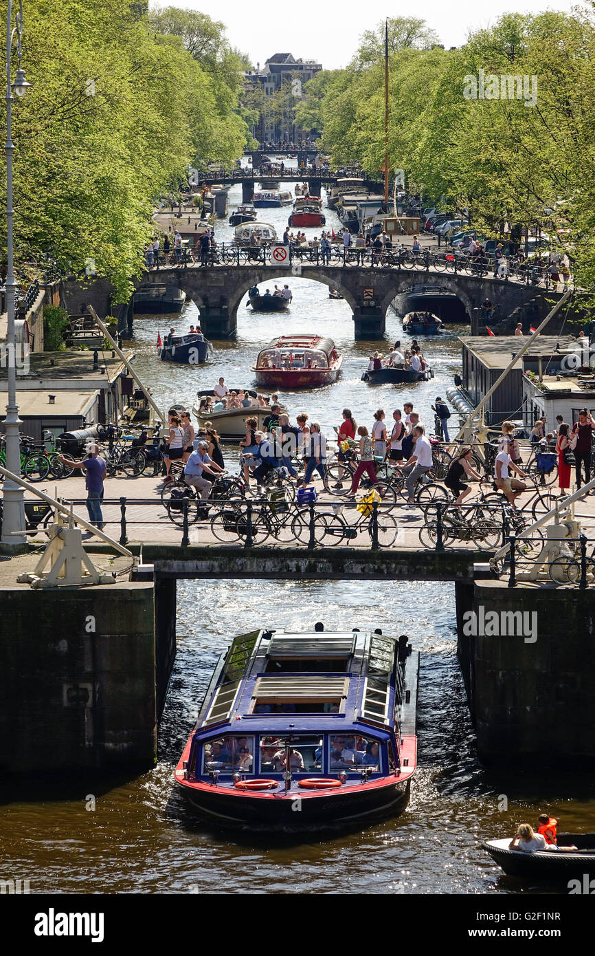 Canali di Amsterdam. Quattro ponti con molti ciclisti sul canale Prinsengracht con canal tour barche e piccole imbarcazioni da diporto in primavera Foto Stock