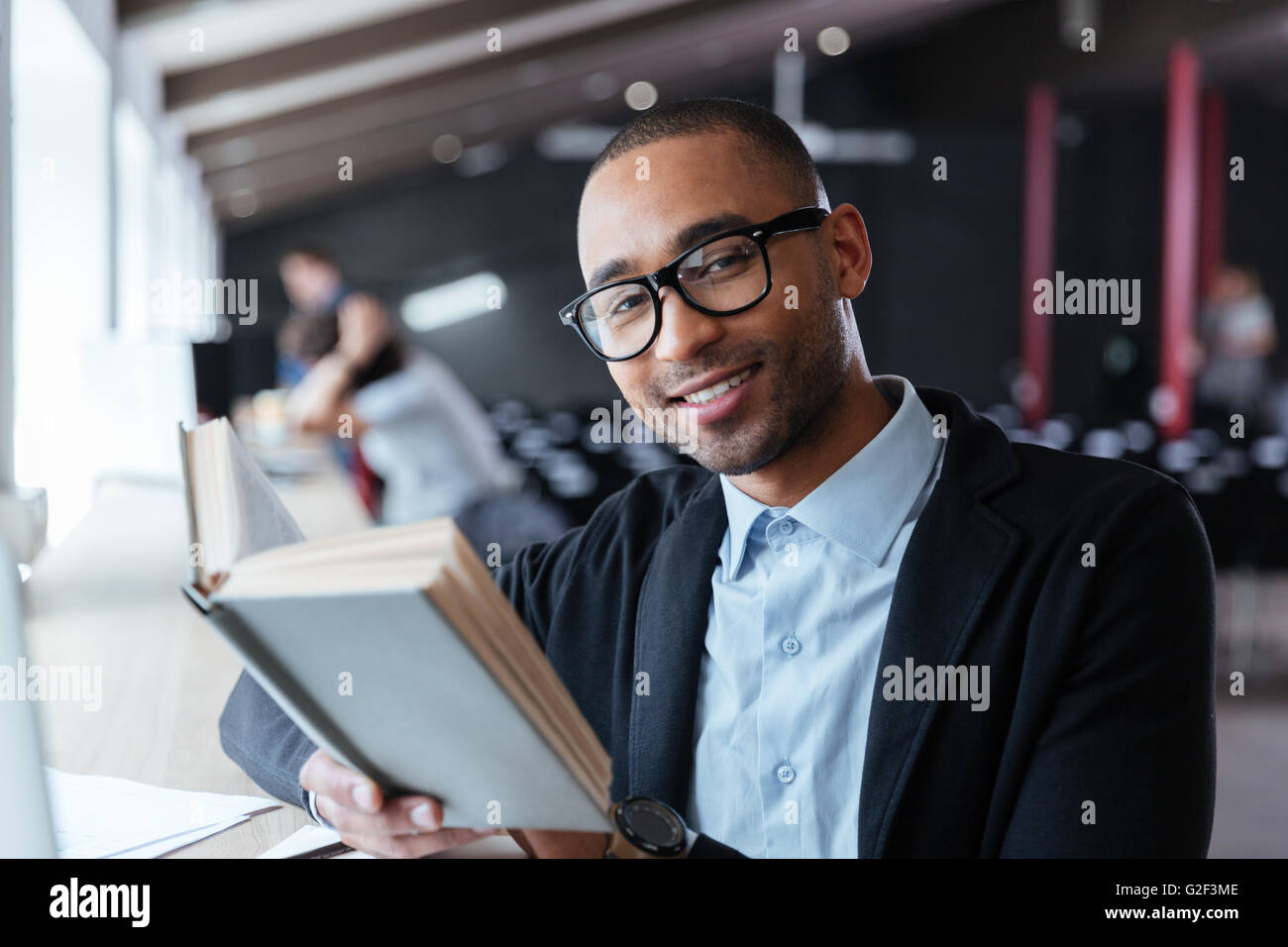 Bel giovane uomo d affari la lettura di un libro alla sua scrivania in ufficio Foto Stock
