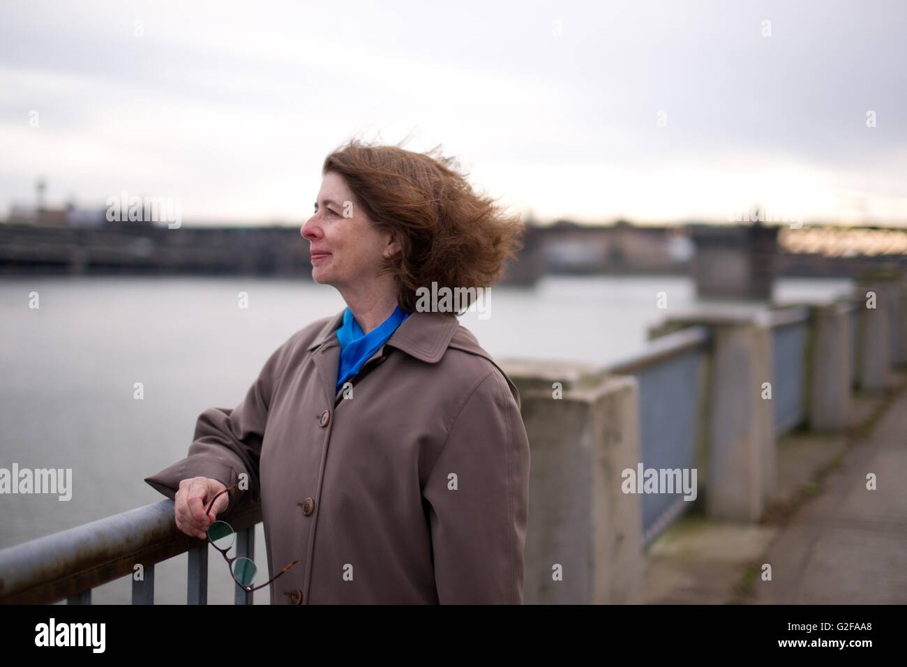 Mid-Adult donna in trench coat braccio di appoggio sulla ringhiera mentre cercano sul fiume Foto Stock