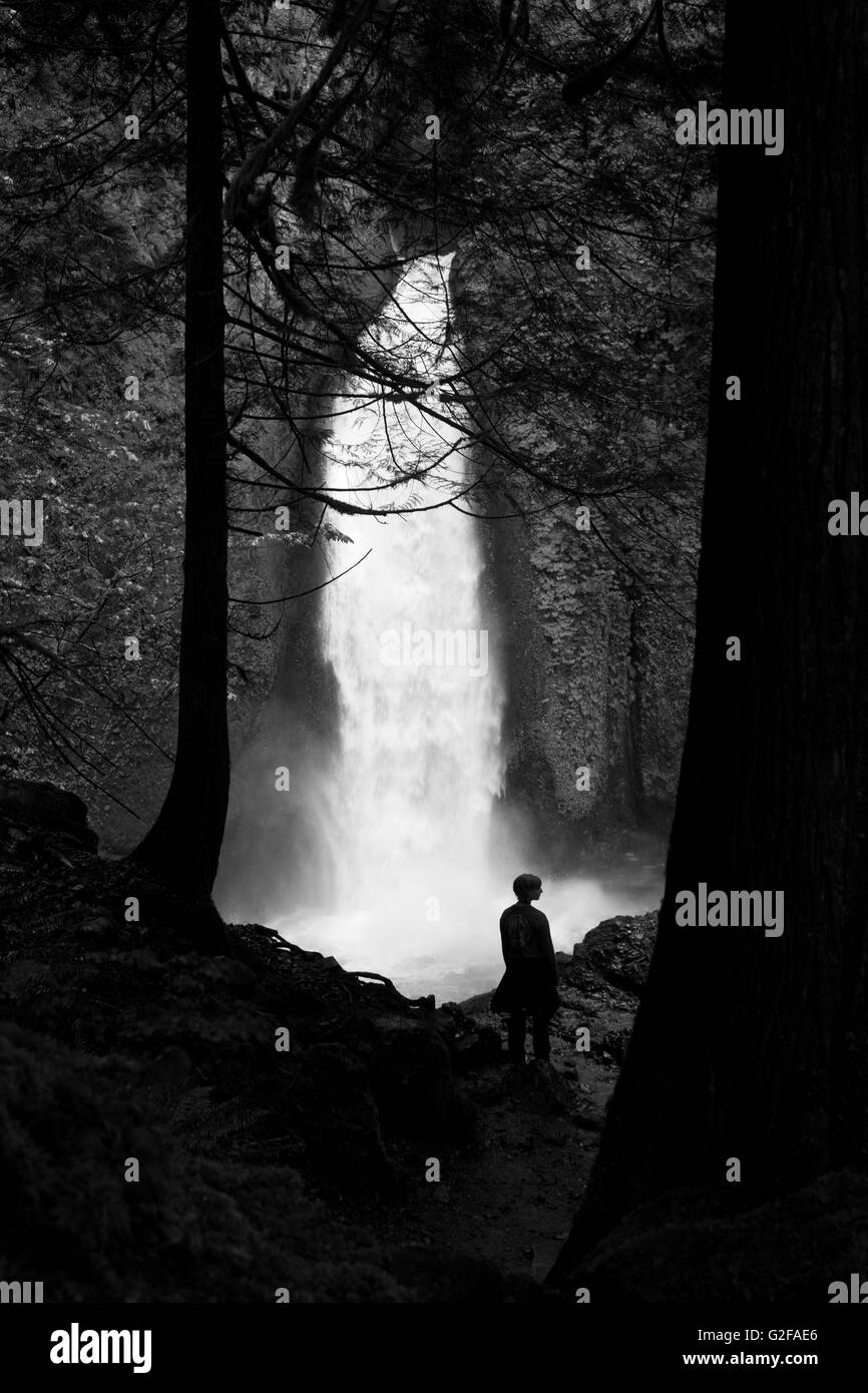 Mid-Adult donna in piedi di fronte a cascata nella foresta Foto Stock