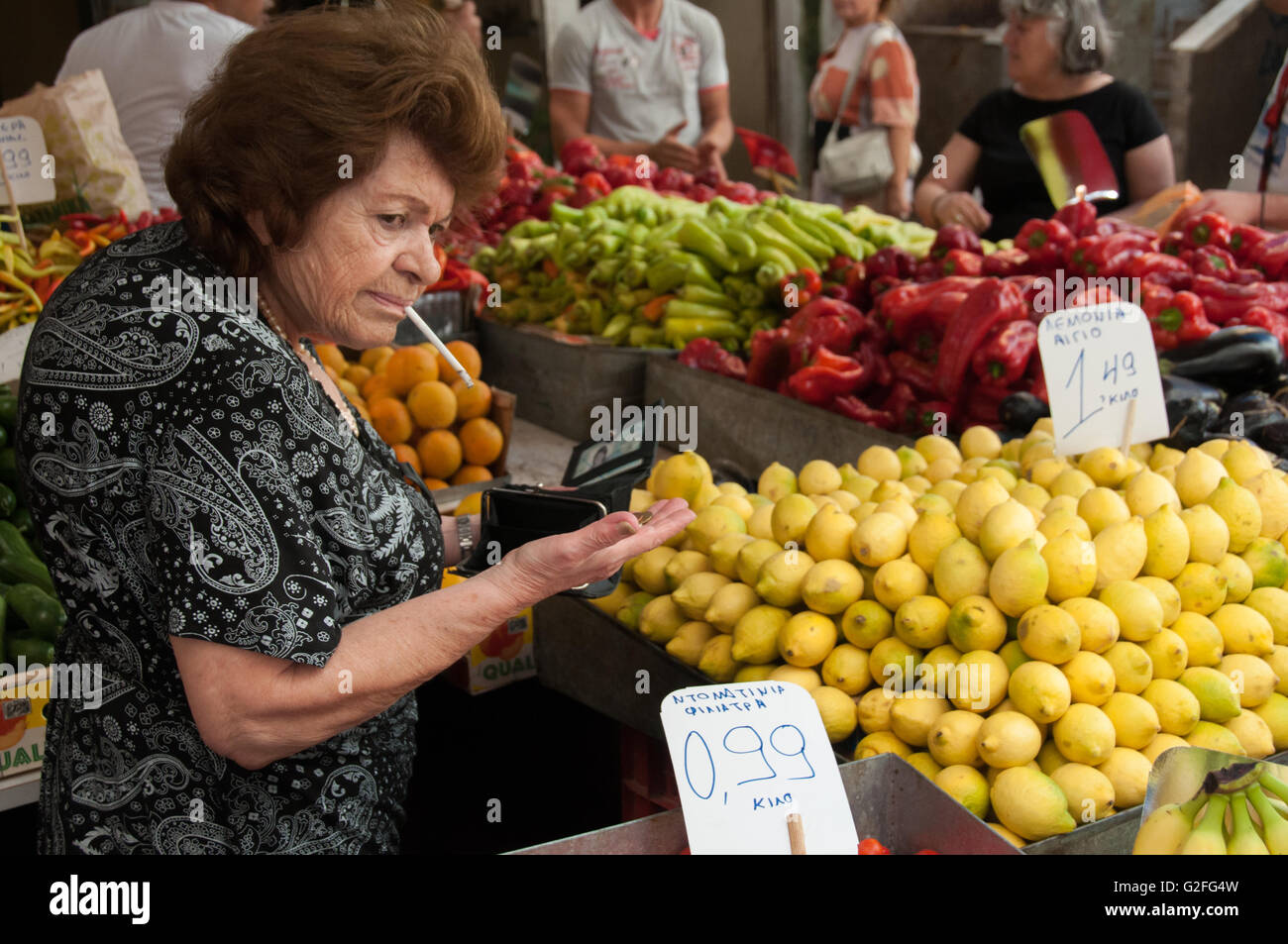 Vecchia donna greca di fumare e la vendita di frutta e verdura in stallo di pesci e di frutta di mercato di strada in Omonia Monastriki Agorà di Atene. Foto Stock