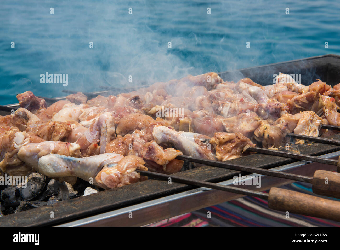 Cosce di pollo disossate di pollo su spiedini cottura su barbecue bbq con oceano tropicale sfondo Foto Stock