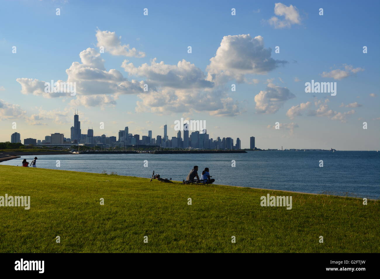 Una coppia fa una pausa sulla pista ciclabile fronte lago sul lato sud del quartiere di Kenwood a Chicago con lo skyline della città sullo sfondo. Foto Stock