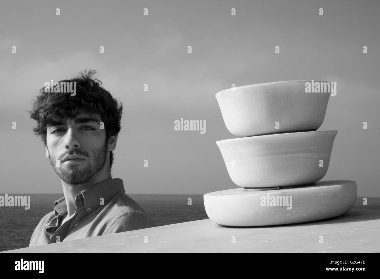 Testa e spalle Ritratto di giovane uomo adulto nei pressi di scultura astratta con Ocean in background Foto Stock