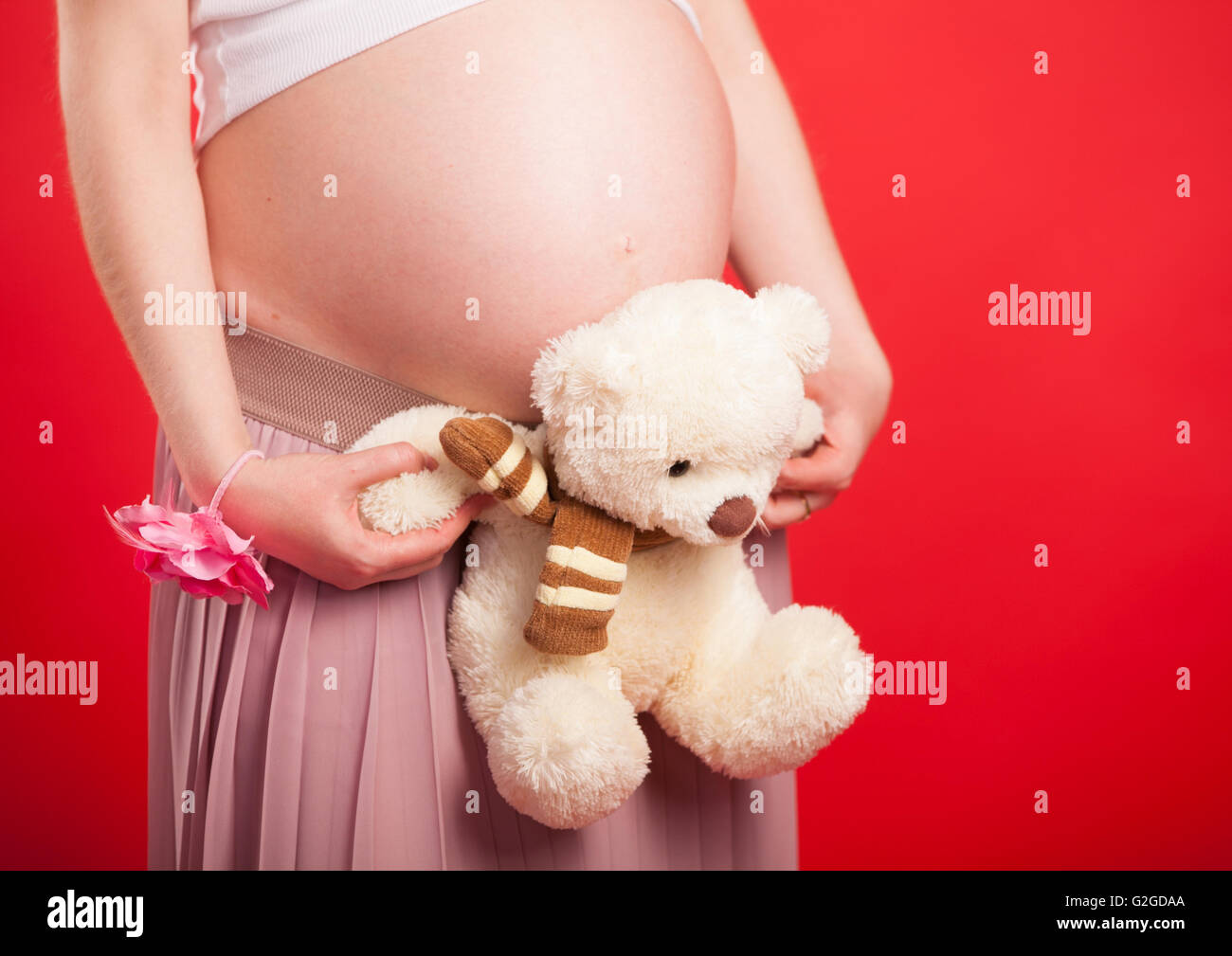 Toy Bear Cub contro un ventre della donna incinta. La donna incinta con un giocattolo Bear Cub sono a piedi su un prato Foto Stock
