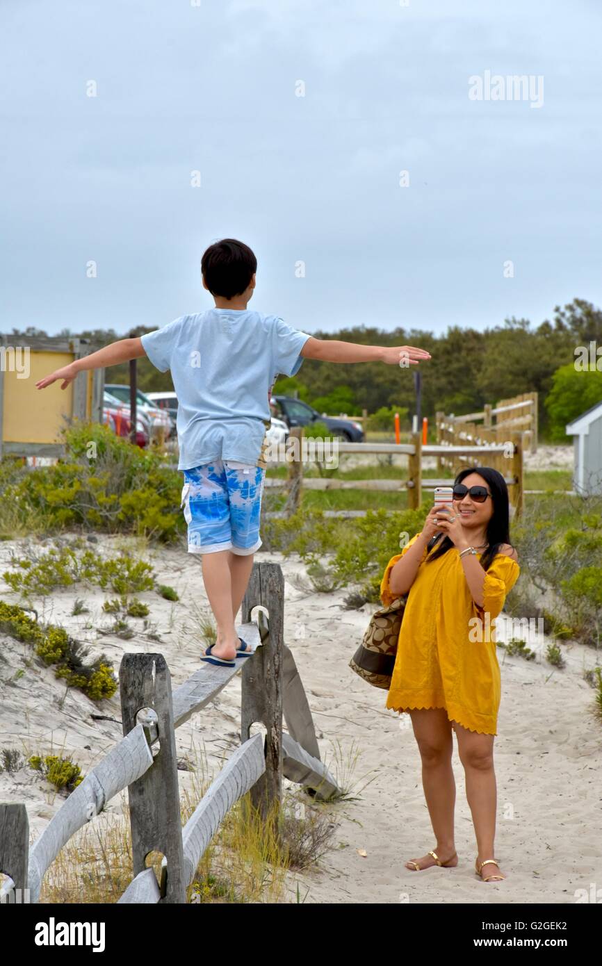 Un giovane ragazzo cerca di equilibrio come egli cammina attraverso la parte superiore di una recinzione di legno in spiaggia Foto Stock