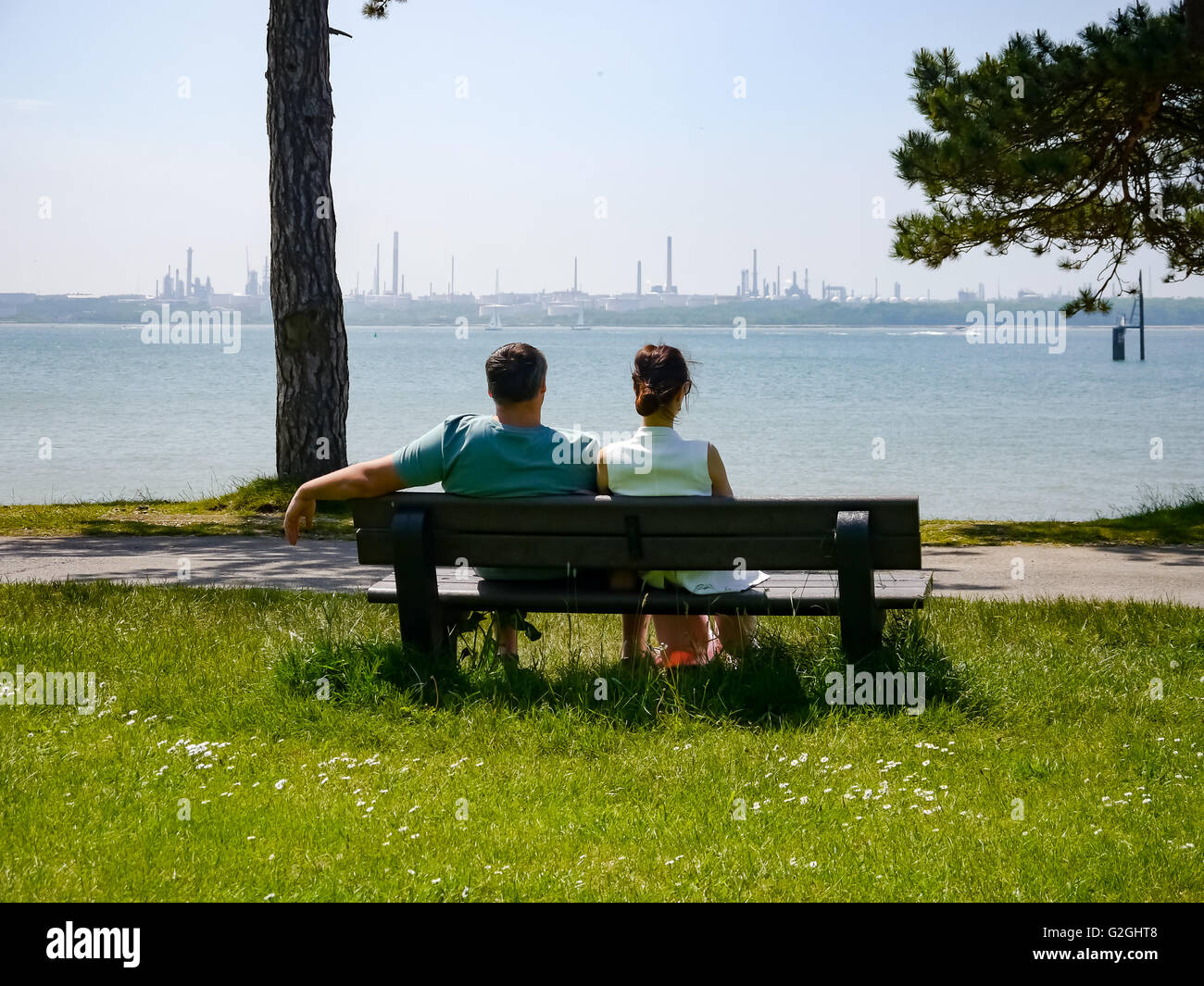 Un maschio e femmina giovane poggiano su una panchina nel parco che si affaccia su Southampton acqua e Fawley raffineria di petrolio Foto Stock