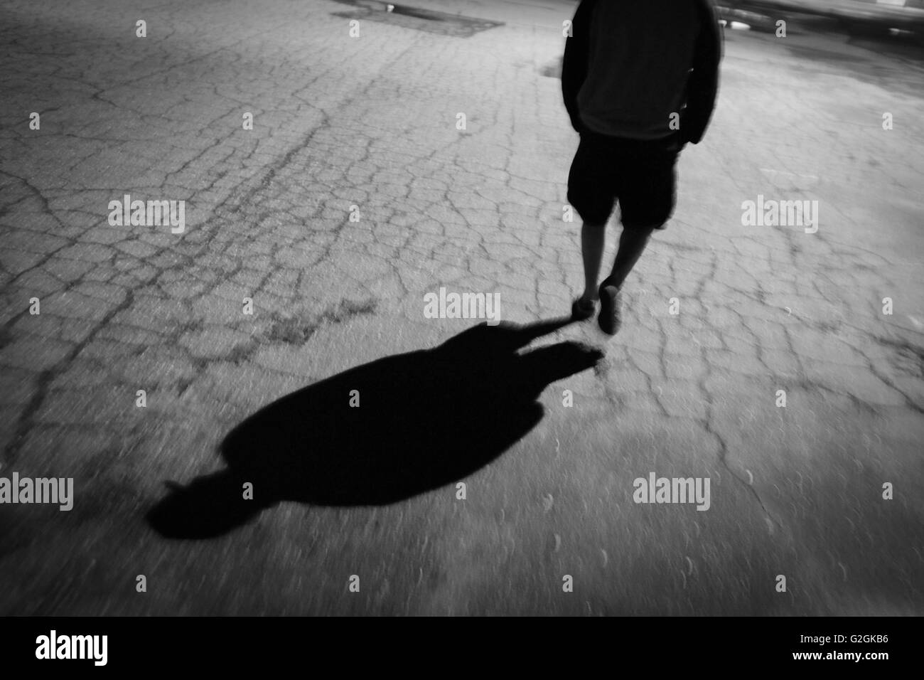Uomo che cammina su asfalto di notte, vista posteriore con ombra Foto Stock