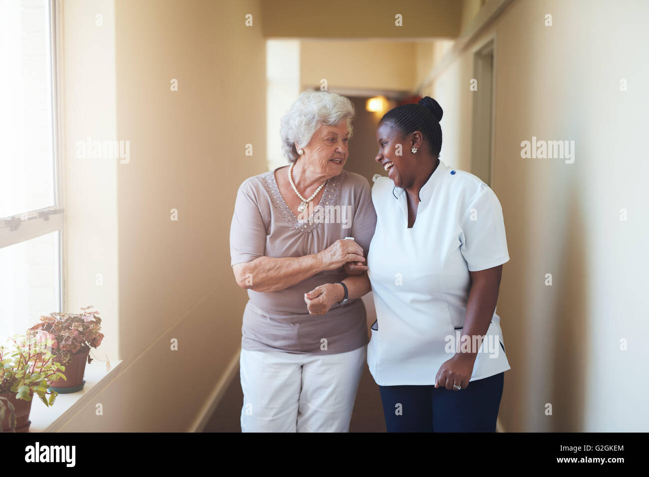 Ritratto di felice caregiver femmina e donna senior camminare insieme a casa. Un operatore sanitario professionale avendo cura di anziani woma Foto Stock