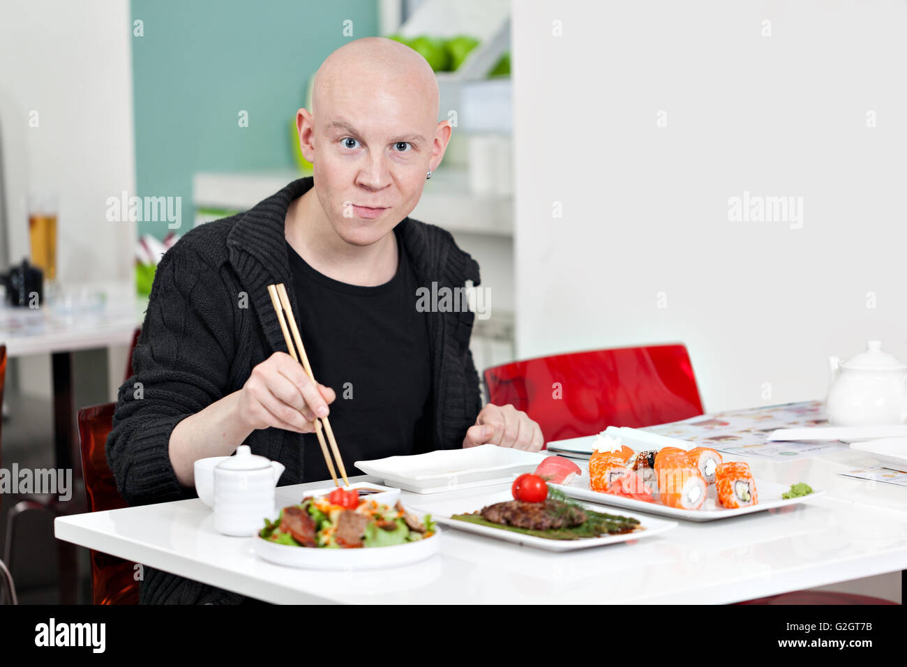 Giovane uomo seduto al sushi bar, sorridente Foto Stock