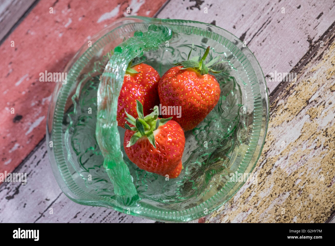 Immagine di overhead di tre fragole in vendemmia verde piatto di vetro su sfondo di legno Foto Stock