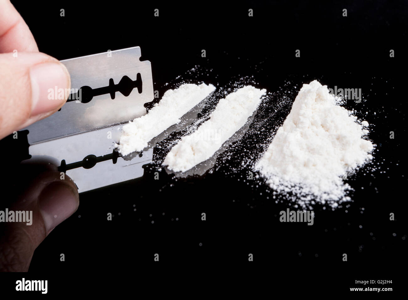 Mano rendendo le righe del farmaco con una lama di rasoio su sfondo nero con la riflessione Foto Stock