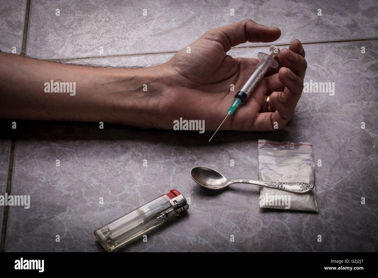 Drog Addict mano con la siringa sul pavimento con un sacco di droghe un cucchiaio e un accendino Foto Stock