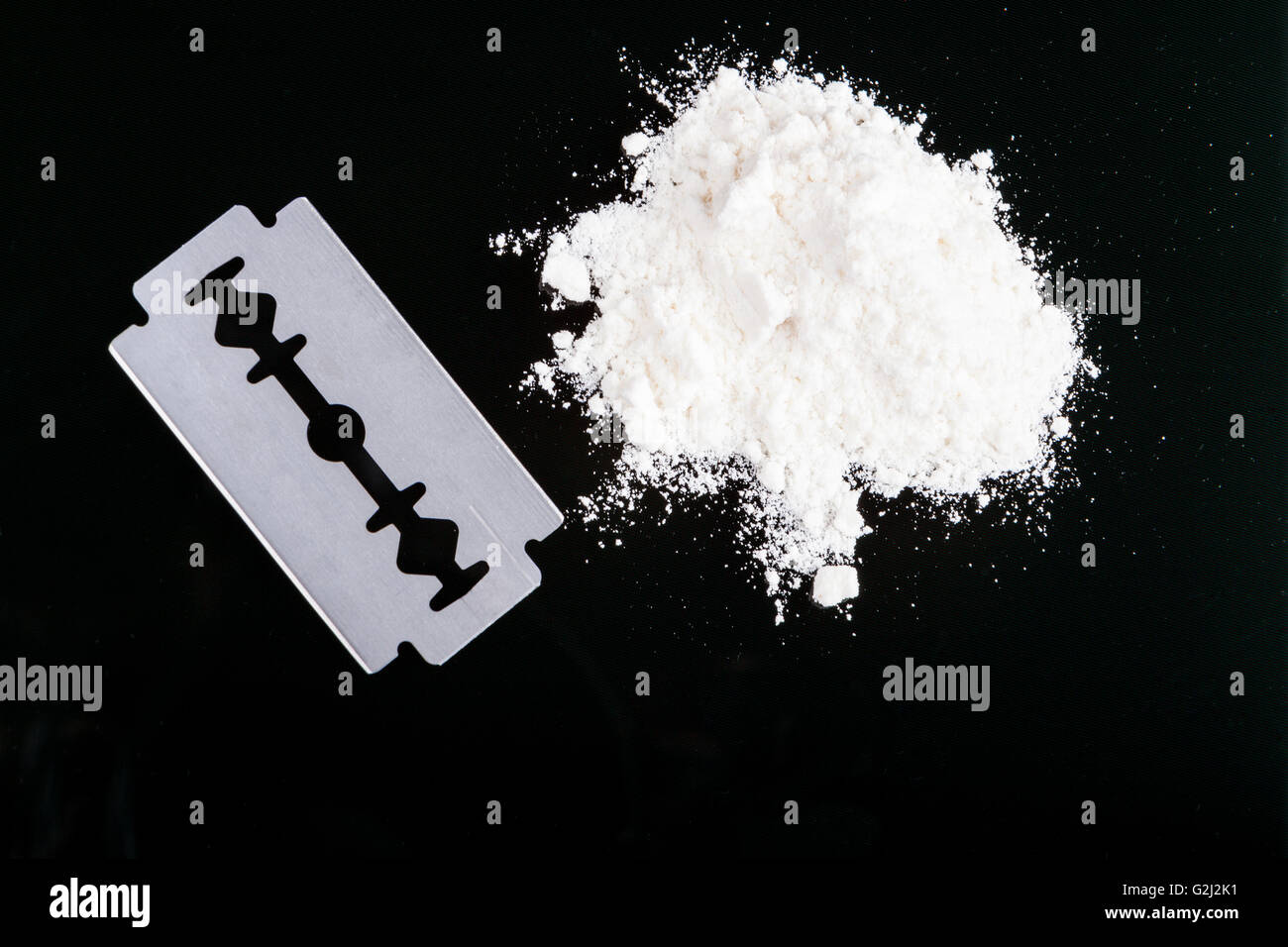 Una lama di rasoio closeup bianco con polvere di farmaco su sfondo nero con la riflessione Foto Stock