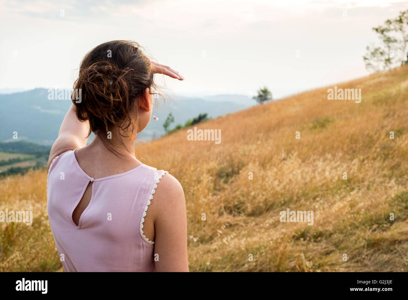 In primo piano della donna in abito rosa guardando fuori nella distanza in campo, vista posteriore Foto Stock