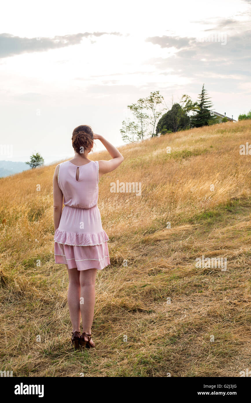 Donna in abito rosa guardando fuori nella distanza in campo, vista posteriore Foto Stock