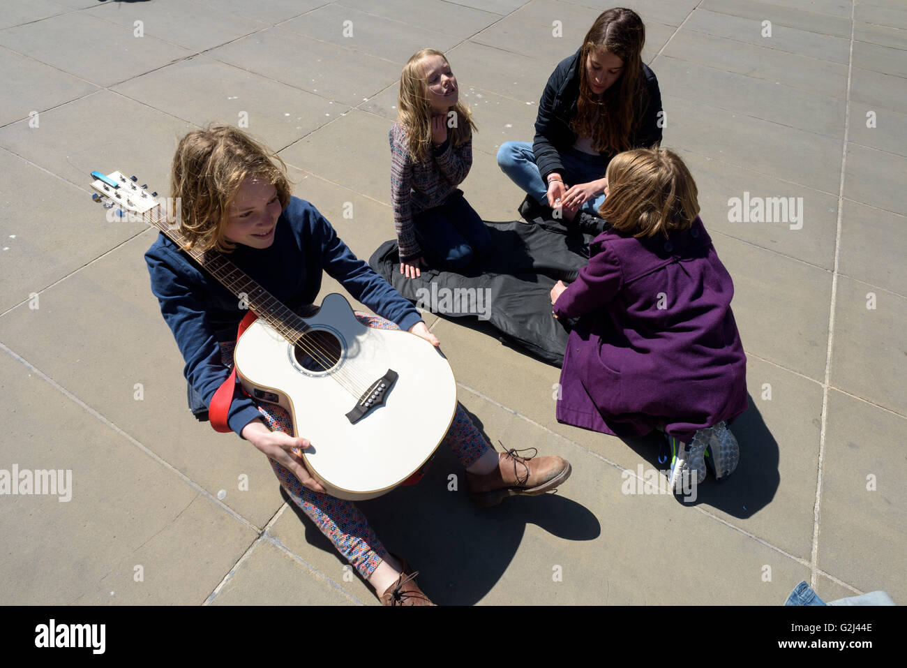 Quattro bambini buskers a sedersi con una chitarra dopo il musicista di strada per denaro in Godliman Street London Foto Stock