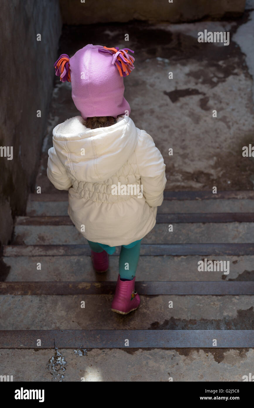 Ragazza giovane con un cappello rosa cammina giù buia e umida passi. La scala non ha alcun parapetti o luci. Foto Stock