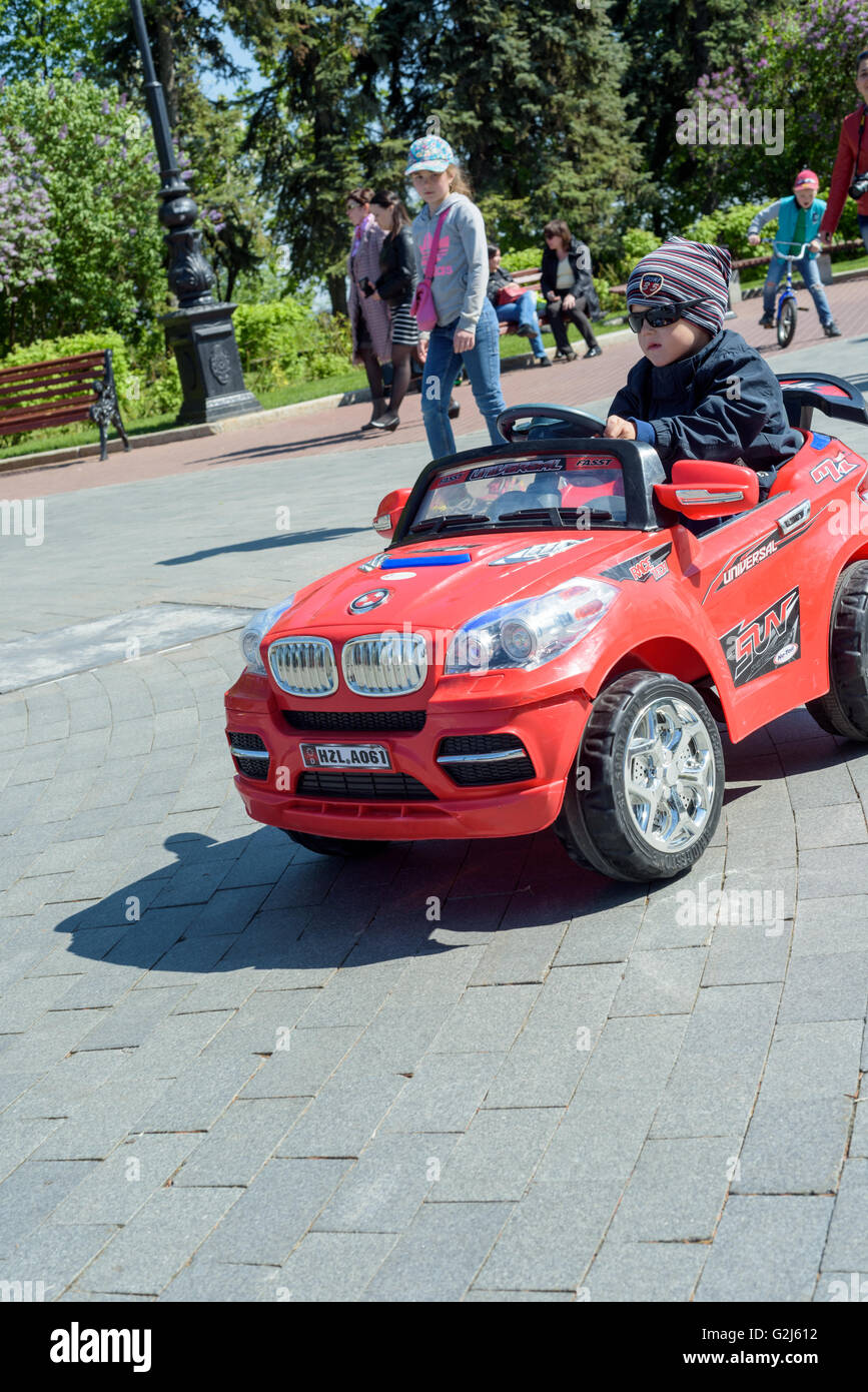 Giovane ragazzo in un cappello e occhiali da sole è divertente in sella a una BMW style con motore elettrico giocattolo auto nella luce del sole. Foto Stock