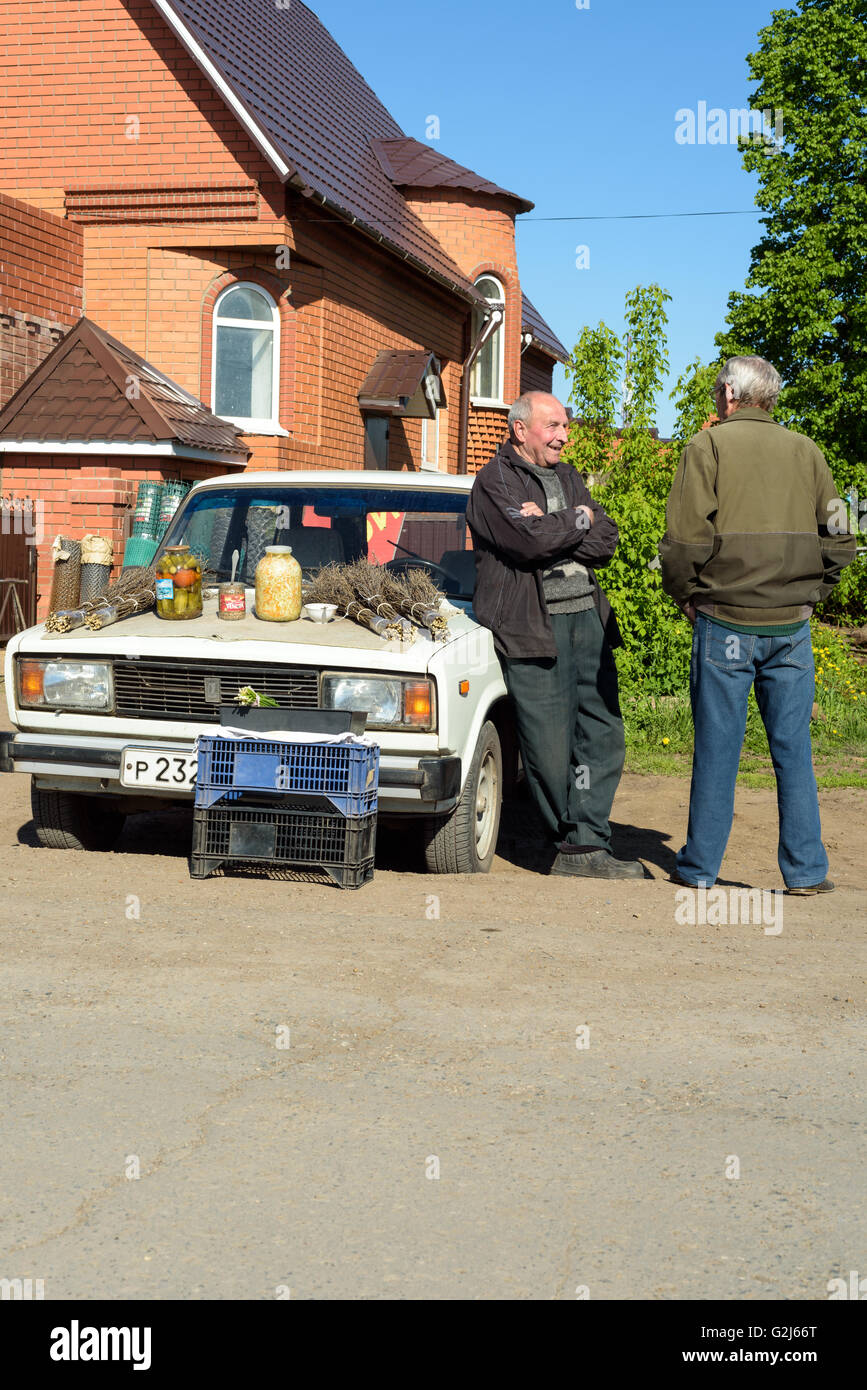 Conversazione tra due uomini insieme con prodotti fatti in casa su un cofano per auto in vendita presso il locale mercato degli agricoltori in Russia Foto Stock