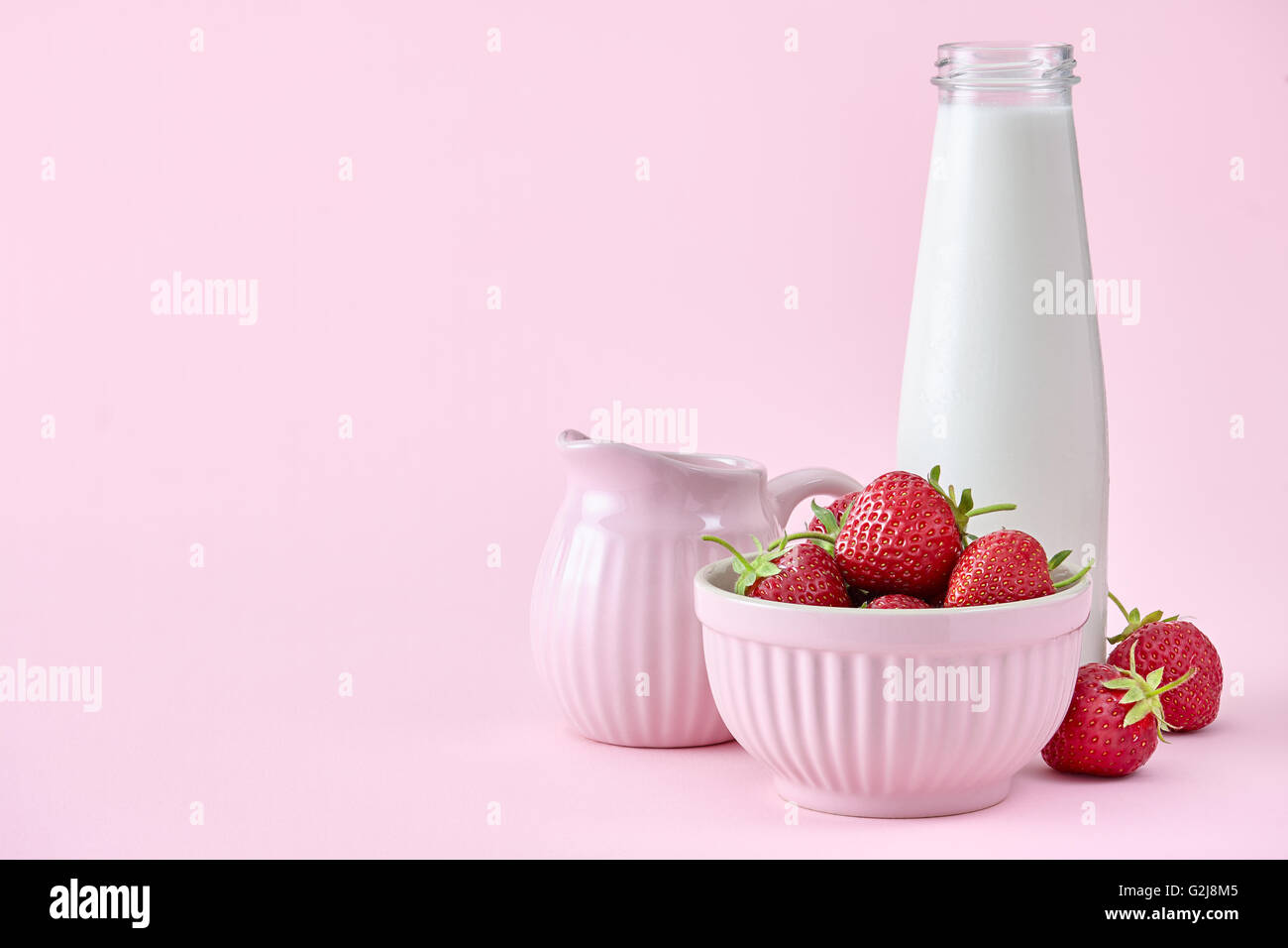 Le fragole in rosa ciotola con bottiglia di latte Foto Stock