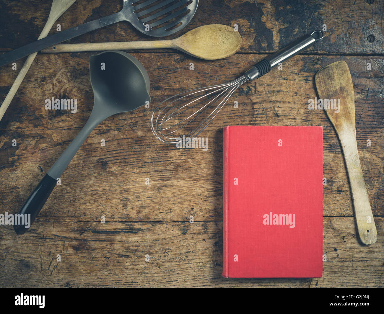 Una selezione di utensili da cucina su un tavolo di legno con un libro Foto Stock