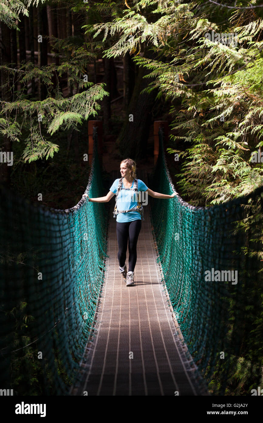 Giovane donna escursionista sulla sospensione ponte tra la Cina e la spiaggia Spiaggia di mistica lungo Juan de Fuca Trail Isola di Vancouver BC Canada. Foto Stock