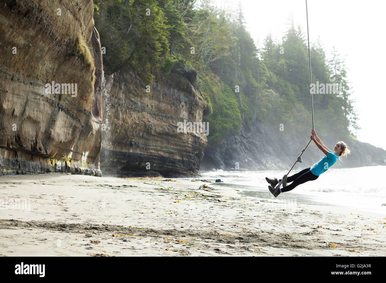 Una giovane donna oscilla su una corda swing di Mystic spiaggia lungo il Juan de Fuca Trail. Isola di Vancouver, BC, Canada. Foto Stock