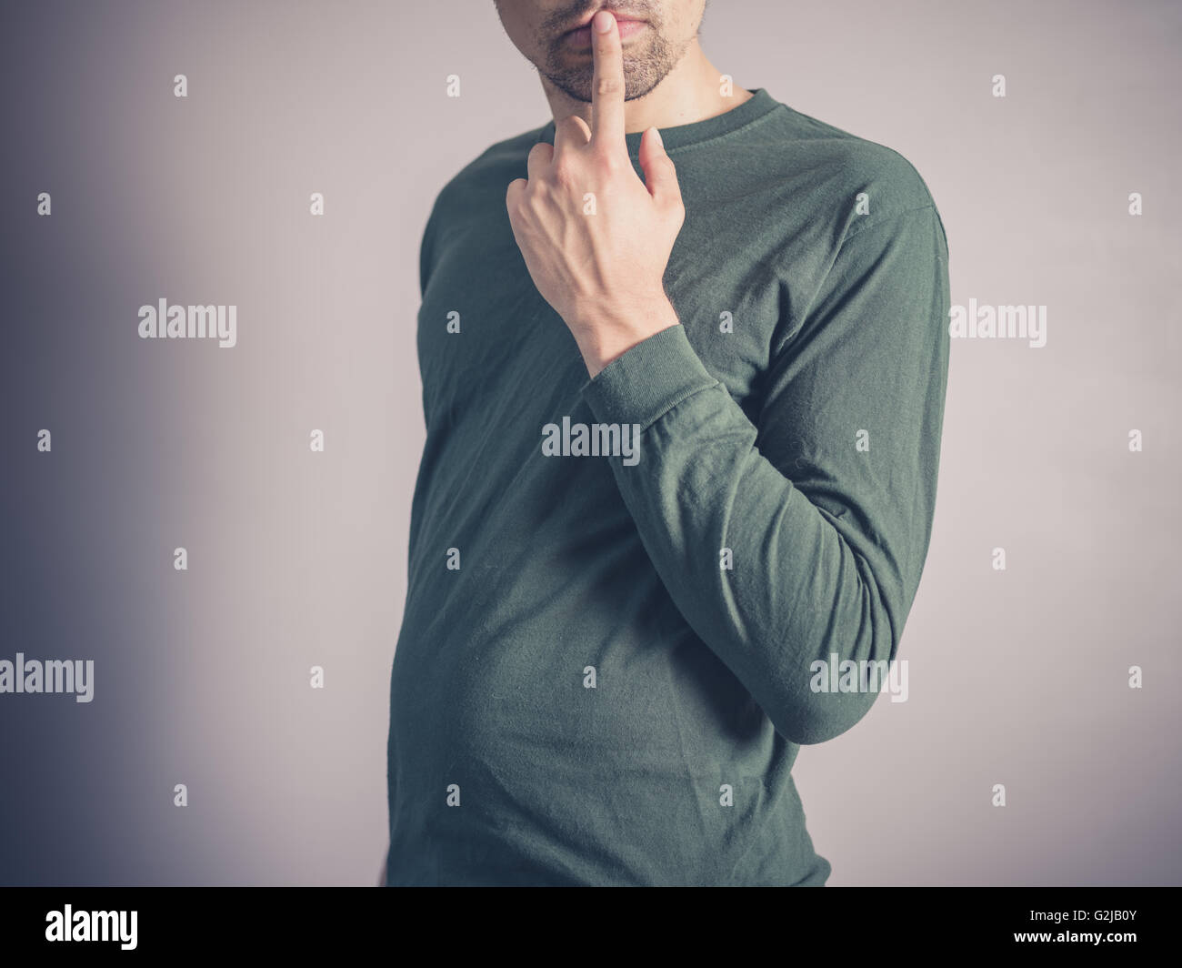 Un giovane uomo che indossa un top verde sta cercando in questione e premuroso con il suo dito sulle sue labbra Foto Stock