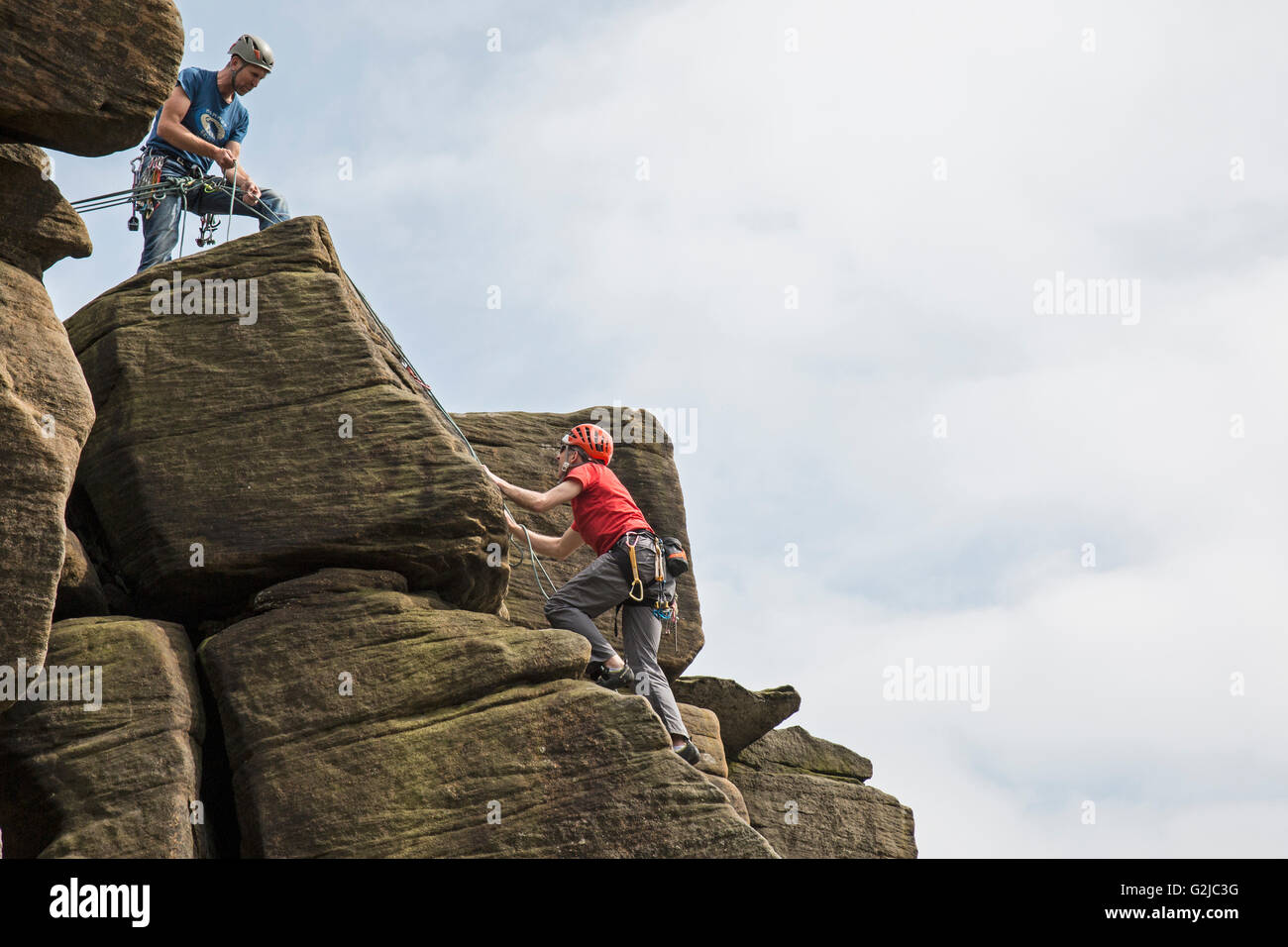 Scalatore sulle scogliere di Stanage Plantation nel Peak District of England. Secondo scalatore nella parte superiore ha una fune di sicurezza. Foto Stock