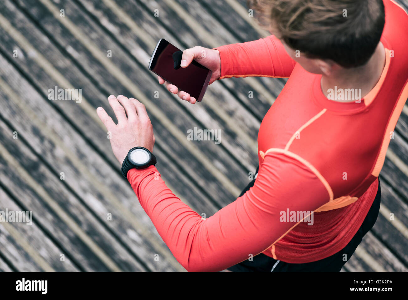 Uomo che corre controllando le prestazioni sportive sul suo telefono mobile e smartwatch app Foto Stock