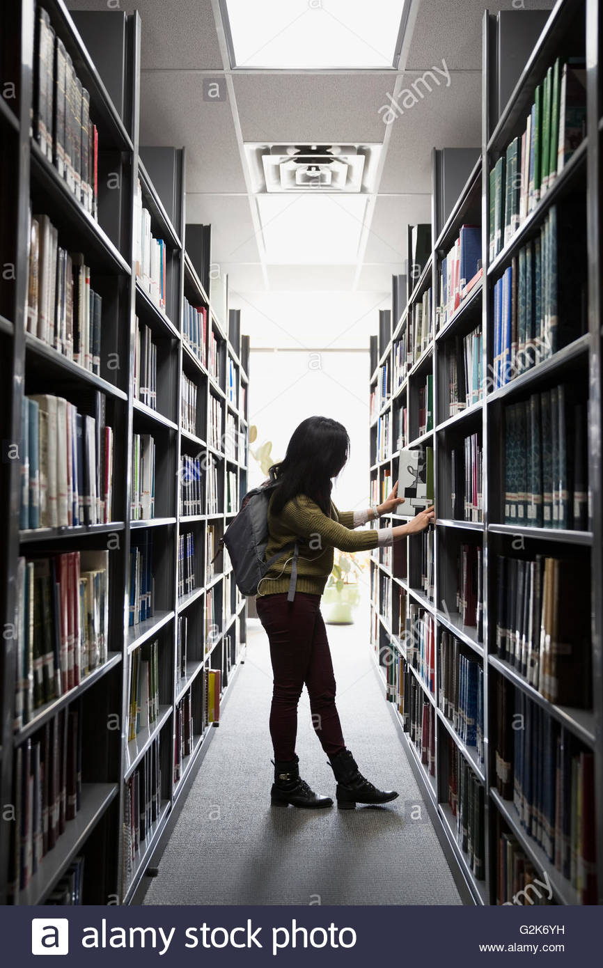 Studente di College alla ricerca di libro in biblioteca Foto Stock