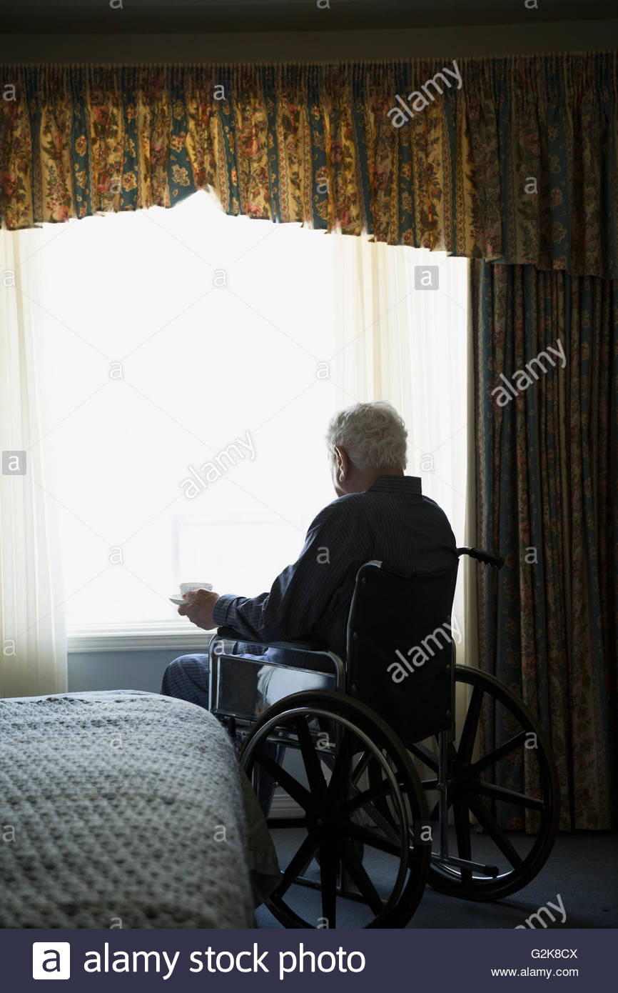Senior uomo in carrozzella bere il tè in corrispondenza della finestra Foto Stock