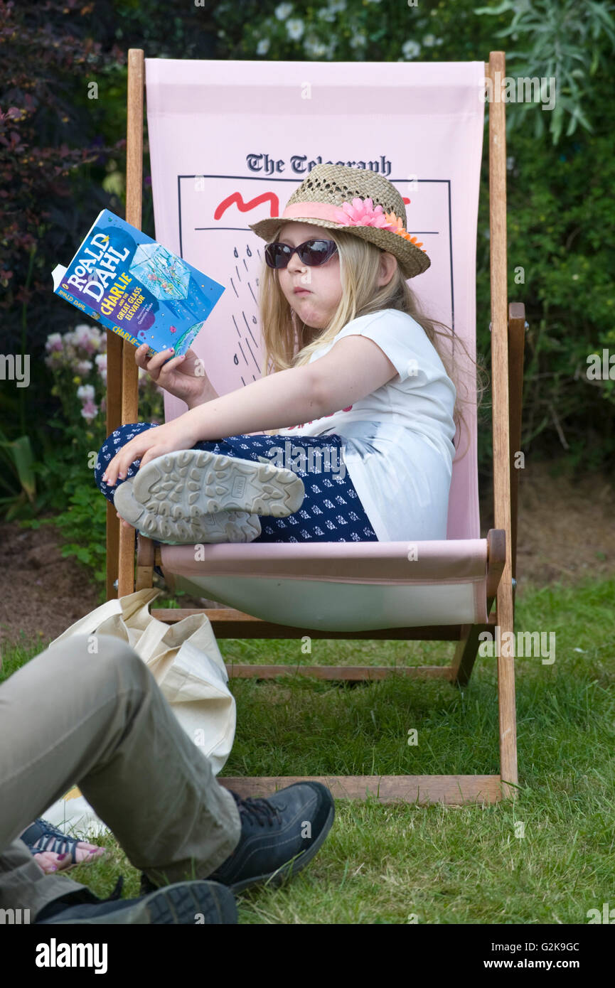 Giovane ragazza seduta in sedia a sdraio leggendo un libro sul prato a Hay Festival 2016 Foto Stock