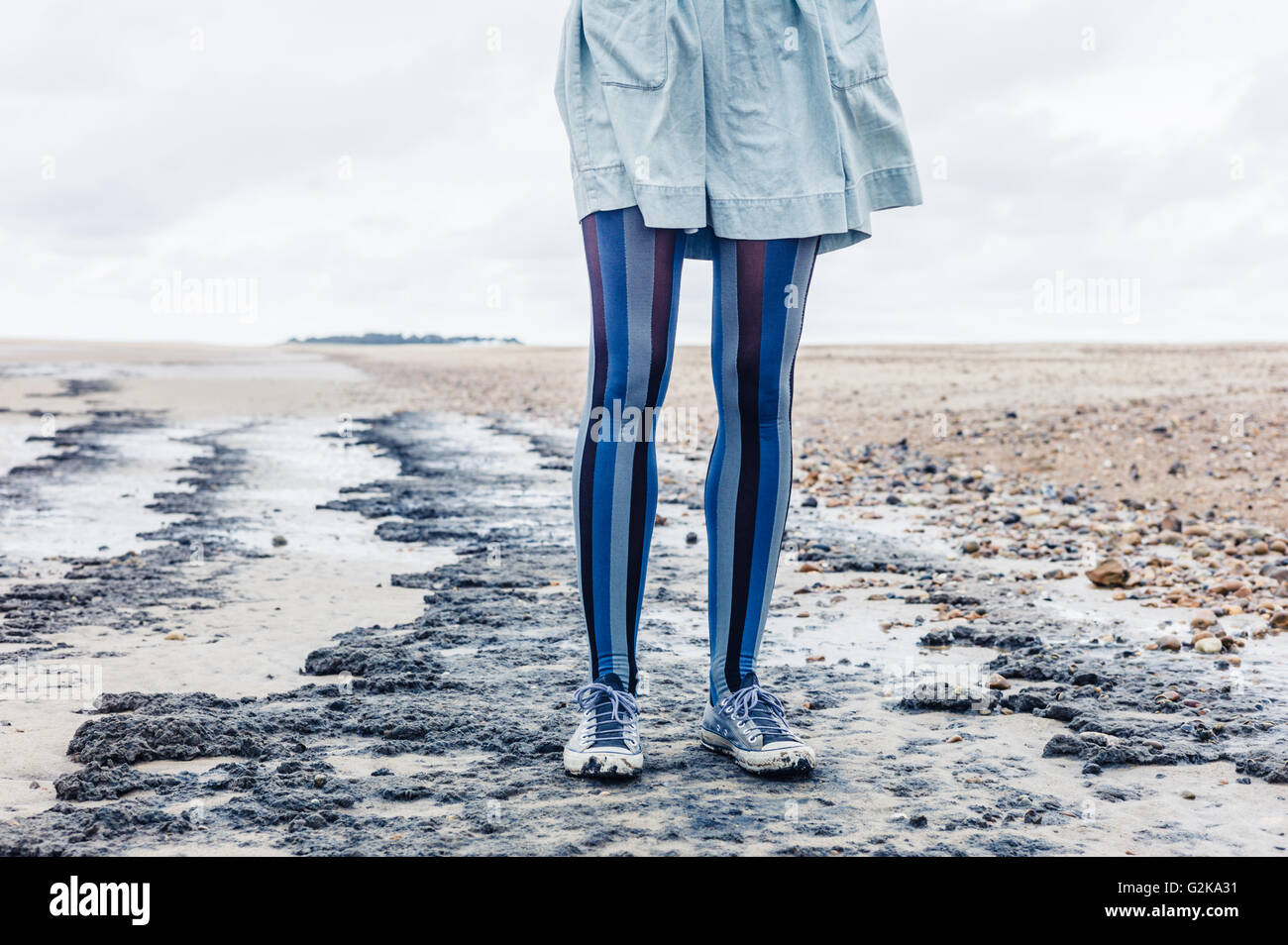 Le gambe di una giovane donna come lei è in piedi sulla spiaggia con il suo mantello al vento Foto Stock