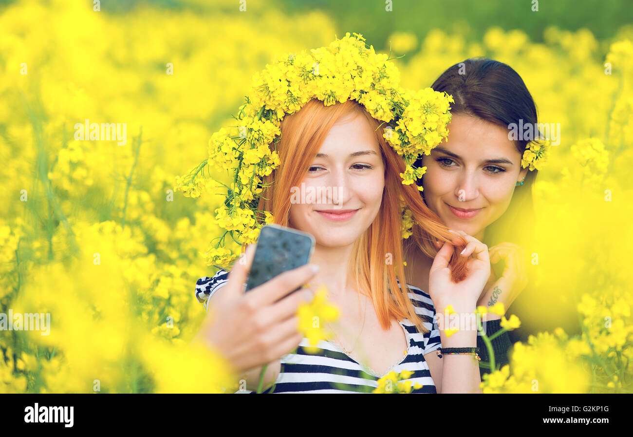 Due amici prendendo un selfie in un campo di fiori gialli di semi di colza Foto Stock
