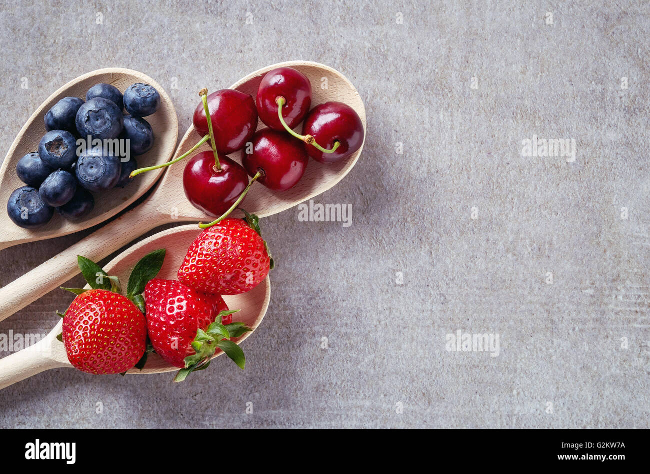 I mirtilli, le ciliegie e fragole in cucchiai di legno sul tavolo di pietra, vista dall'alto Foto Stock